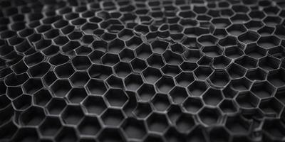 The primary subject of the image is a close-up of a black, hexagonal pattern. The setting is a black background, which contrasts with the pattern. The visual style is a close-up of a textured surface, possibly a piece of fabric or a wallpaper with a hexagonal pattern. The colors and mood of the image are predominantly black, giving it a bold and striking appearance.