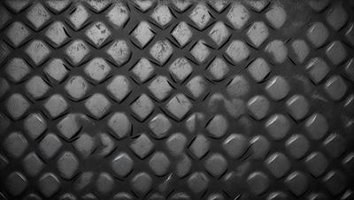 The primary subject of the image is a close-up of a black, textured surface with a pattern of small circles. The setting appears to be a dark room, and the visual style is a black and white photo. The dominant colors are black and white, and the overall atmosphere is somewhat mysterious and intriguing.