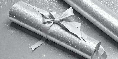 The primary subject of the image is a white bow, which is tied around a package. The setting is a silver background, and the visual style appears to be a photo. The colors and mood of the image are predominantly white, giving it a clean and elegant appearance.