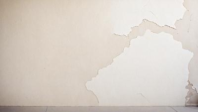 The primary subject of the image is a wall with a large crack in it. The setting is a room with a white wall, and the visual style appears to be a photo. The colors and mood of the image are predominantly white, giving it a clean and minimalist appearance.