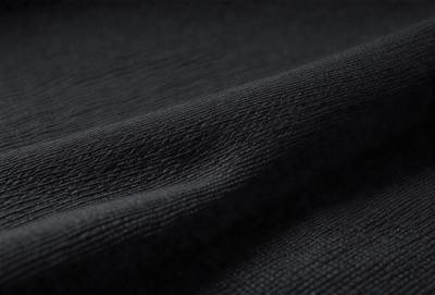 The primary subject of the image is a black fabric, which appears to be a piece of clothing or a curtain. The setting is a dark room, and the visual style is a close-up of the fabric. The colors and mood of the image are predominantly dark and moody, with the black fabric being the main focus.