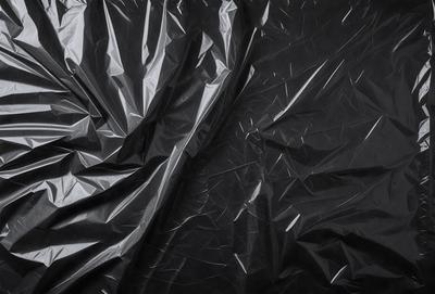 The primary subject of the image is a black plastic bag. The setting is a dark room, and the visual style is a close-up of the plastic bag. The colors and mood of the image are predominantly dark, with the black plastic bag being the main focus.
