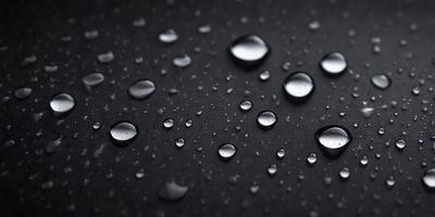The primary subject of the image is a close-up of a black surface with water droplets on it. The setting is a dark background, and the visual style appears to be a photo. The colors in the image are predominantly black and white, with the water droplets adding a touch of silver. The overall atmosphere is moist and reflective.
