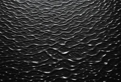 The primary subject of the image is a large body of water, which appears to be a black ocean. The setting is a vast expanse of water, with no visible land or other objects. The visual style of the image is a black and white photo, which adds a sense of depth and contrast to the scene. The colors and mood of the image are predominantly dark and moody, with the water's surface reflecting the surrounding environment.