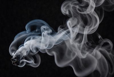 The primary subject of the image is a cigarette, which is the main focus of the scene. The setting is a dark background, which creates a moody atmosphere. The visual style is a close-up of the cigarette, emphasizing its details. The colors in the image are predominantly shades of gray, which contribute to the overall mood of the scene.