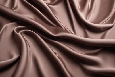 The primary subject of the image is a close-up of a piece of fabric, possibly a silk or satin material. The setting is a room with a wall, and the visual style appears to be a photo. The colors in the image are predominantly brown, giving the scene a warm and cozy atmosphere.