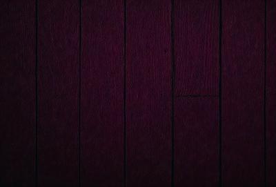 The primary subject of the image is a wooden floor with a purple color. The setting is a room with a wooden wall, and the visual style is a close-up of the wooden floor. The colors and mood of the image are predominantly purple, creating a calm and serene atmosphere.