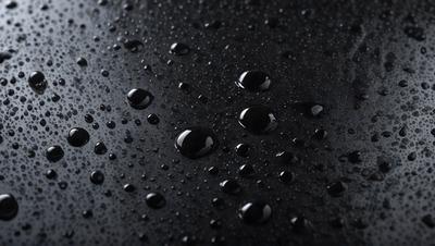 The primary subject of the image is a close-up of a black surface with numerous small droplets of water on it. The setting appears to be a dark room, and the visual style is a black and white photo. The dominant colors are black and white, and the overall atmosphere is moody and dramatic.