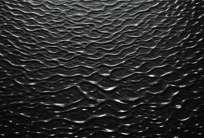 The primary subject of the image is a large body of water, which appears to be a black ocean. The setting is a vast expanse of water, with no visible land or other objects. The visual style of the image is a black and white photo, which adds a sense of depth and contrast to the scene. The colors and mood of the image are predominantly dark and moody, with the water's surface reflecting the surrounding environment.