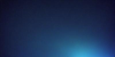 The primary subject of the image is a star, which is located in the middle of the night sky. The setting is a dark, cloudy night with a blue background. The visual style is a photo, capturing the star in its natural environment. The colors and mood of the image are predominantly dark and moody, with the star being the only bright and prominent feature in the sky.