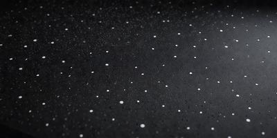 The primary subject of the image is a black background with white specks or dots scattered across it. The setting appears to be a dark room, and the visual style is a close-up of the black background with the white specks. The colors and mood of the image are predominantly dark and moody, with the white specks adding a touch of contrast and interest to the overall composition.