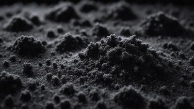 The primary subject of the image is a black substance, possibly a powder or a dark substance, with a texture that resembles a mountain. The setting is a black background, which contrasts with the black substance. The visual style appears to be a close-up of the substance, showcasing its texture and appearance. The colors and mood of the image are predominantly dark, with the black substance being the main focus.