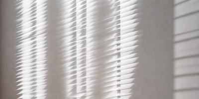 The primary subject of the image is a white shade or blind, which is covering a window. The setting is indoors, with the window being the main focus of the image. The visual style appears to be a photo, as it captures the light shining through the shade and creating a pattern on the wall. The colors in the image are predominantly white, giving it a clean and minimalist appearance.