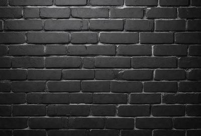 The primary subject of the image is a black brick wall. The setting is a brick wall, and the visual style is a photo. The dominant colors are black and grey, creating a moody atmosphere.