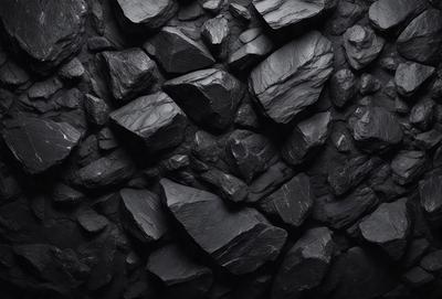 The primary subject of the image is a large pile of black rocks. The setting is a dark room, possibly a cave or a black and white photo. The visual style is a black and white photo, giving the image a classic and dramatic appearance. The dominant colors are black and white, creating a moody and dramatic atmosphere.