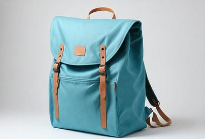 The primary subject of the image is a blue backpack with a brown strap. The backpack is placed on a white background, giving it a clean and minimalist appearance. The visual style of the image is a photo, capturing the details of the backpack and its strap. The colors and mood of the image are predominantly blue and white, creating a calm and serene atmosphere.