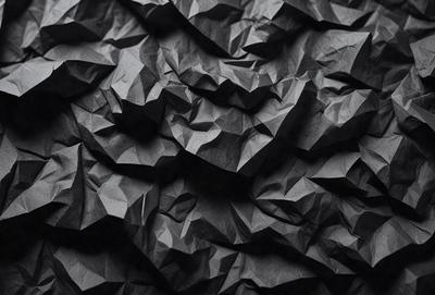 The primary subject of the image is a black and white patterned surface, which appears to be a piece of fabric or a wallpaper design. The setting is a dark room, and the visual style is a close-up of the patterned surface. The colors and mood of the image are predominantly dark and moody, with the black and white pattern adding a sense of depth and intricacy to the scene.