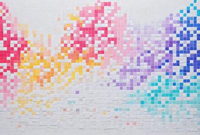 The primary subject of the image is a colorful mosaic made of small squares. The setting is a white wall, and the visual style is a combination of digital art and illustration. The mosaic features a variety of colors, creating a vibrant and lively atmosphere.