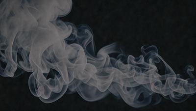 The primary subject of the image is a cloud of smoke, which is the main object, scene, or focus of the image. The setting is a dark background, which contrasts with the smoke. The visual style is a black and white photo, giving the image a classic and timeless appearance. The colors and mood are dominated by the smoke, which creates a dramatic and moody atmosphere.