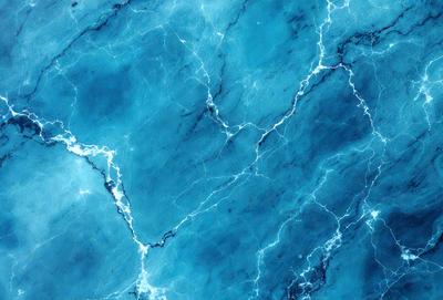 The primary subject of the image is a blue marble-like surface with a pattern of white streaks. The setting is a blue background, which creates a striking contrast with the blue marble. The visual style is a close-up of the marble, showcasing its unique texture and pattern. The colors and mood of the image are predominantly blue, with the white streaks adding a touch of contrast and interest to the overall composition.