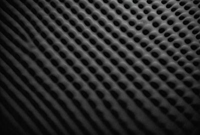 The primary subject of the image is a black and white patterned surface, which appears to be a textured material or a patterned fabric. The setting is a dark background, which contrasts with the patterned surface. The visual style of the image is a close-up of the patterned surface, showcasing its intricate details. The colors and mood of the image are predominantly black and white, giving it a classic and timeless appearance.