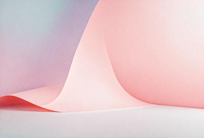 The primary subject of the image is a large piece of pink paper. The setting is a white background, which provides a clean and minimalist appearance. The visual style is a close-up of the paper, showcasing its texture and color. The dominant colors are pink and white, creating a warm and inviting atmosphere.