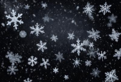 The primary subject of the image is a snowy scene with a dark background. The setting is a winter landscape, possibly a nighttime cityscape, as the snowflakes are falling in the air. The visual style is a black and white photo, which adds a sense of nostalgia and timelessness to the scene. The dominant colors are white and black, creating a stark contrast between the snowflakes and the dark background. The overall atmosphere is serene and peaceful, as the snowflakes gently fall and create a beautiful winter scene.