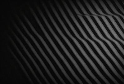 The primary subject of the image is a black and white striped pattern. The setting is a dark background, which contrasts with the pattern. The visual style is a black and white photo, giving it a classic and timeless appearance. The colors and mood of the image are predominantly dark and moody, with the contrasting light and dark stripes creating a sense of depth and intrigue.