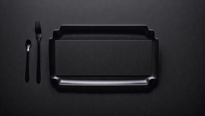 The primary subject of the image is a black tray or container. The setting is a black background, which creates a contrast with the tray. The visual style is a close-up of the tray, showcasing its details. The colors and mood of the image are dark and moody, with the black tray being the main focus.