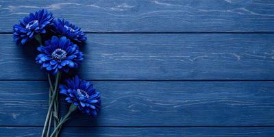 The primary subject of the image is a bouquet of blue flowers. The flowers are placed on a blue wooden surface, which could be a table or a wall. The setting appears to be a room with a blue color scheme, creating a calm and serene atmosphere. The visual style of the image is a close-up of the flowers, emphasizing their beauty and vibrant colors.