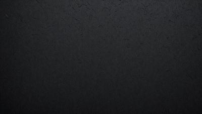 The primary subject of the image is a black background with a texture that resembles a piece of fabric. The setting is a dark room, and the visual style is a close-up of the fabric. The colors and mood of the image are predominantly dark and moody, with the black background and the fabric texture creating a dramatic and mysterious atmosphere.