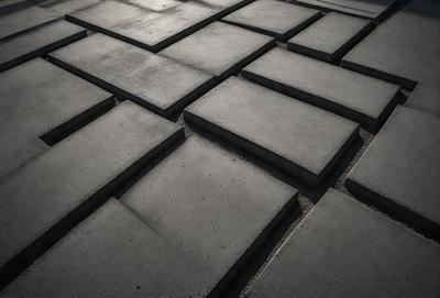 The primary subject of the image is a large, square, concrete block. The setting is a cement floor, and the visual style is a black and white photo. The colors and mood of the image are predominantly dark, with the concrete block being the main focal point.