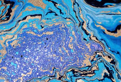 The primary subject of the image is a blue and gold swirling pattern, which appears to be a piece of art or a decorative surface. The setting is a blue background, which complements the vibrant colors of the swirling pattern. The visual style of the image is a mix of artistic and digital elements, creating a unique and eye-catching design. The dominant colors in the image are blue and gold, with the gold accents adding a touch of warmth and sophistication to the overall atmosphere.