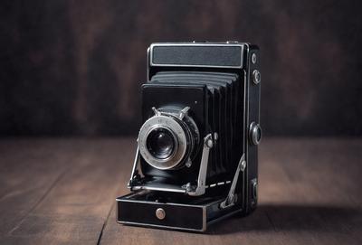 Primary subject: A black and silver camera.

Setting/background: A wooden table.

Visual style: A photo.

Colors and mood: The camera is black and silver, giving it a classic and timeless appearance. The wooden table adds a warm and natural touch to the scene.