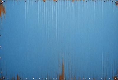 The primary subject of the image is a blue metal surface with rust stains. The setting is an outdoor environment, and the visual style is a photo. The dominant colors are blue and rust, creating a mood of aged and weathered material.