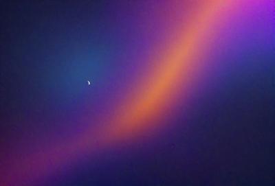 The primary subject of the image is a moon, which is located in the upper left corner of the frame. The setting is a dark, starry sky, with the moon being the main focus. The visual style appears to be a photo, capturing the beauty of the night sky. The colors and mood of the image are predominantly dark and moody, with the moon and stars being the main sources of light.