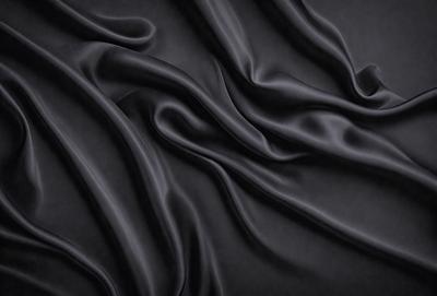 The primary subject of the image is a black fabric, which appears to be a piece of silk. The setting is a dark background, which contrasts with the fabric. The visual style is a close-up of the fabric, showcasing its texture and details. The colors and mood of the image are predominantly dark, with the black fabric being the main focus.
