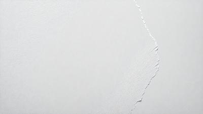 The primary subject of the image is a white wall with a large crack in it. The setting is indoors, and the visual style appears to be a photo. The colors in the image are predominantly white, giving it a clean and minimalist appearance. The mood of the image is somewhat dramatic due to the presence of the large crack in the wall.
