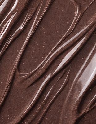 The primary subject of the image is a close-up of a chocolate-colored substance, possibly a chocolate sauce or a chocolate-covered surface. The setting is a brown background, which complements the chocolate color. The visual style appears to be a close-up of a textured surface, possibly a chocolate-covered item or a chocolate sauce. The colors and mood of the image are predominantly brown, creating a warm and rich atmosphere.