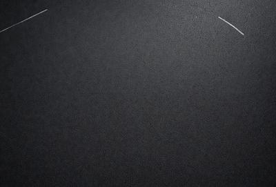 The primary subject of the image is a black surface, which appears to be a carpet or a blacktop. The setting is a dark room, and the visual style is a black and white photo. The colors and mood of the image are predominantly dark and moody, with a sense of mystery or intrigue.