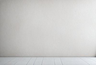 The primary subject of the image is a white wall with a wooden floor. The setting is a room with a blank wall, and the visual style is a photo. The colors and mood of the image are predominantly white, giving it a clean and minimalist appearance.