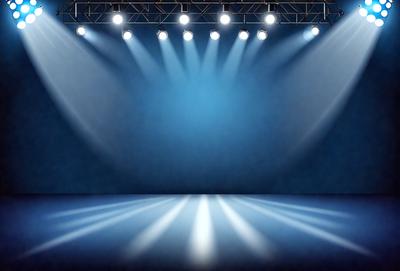 The primary subject of the image is a stage with a blue background. The stage is illuminated by a series of lights, creating a dramatic and theatrical atmosphere. The visual style of the image is a photo, capturing the lighting and stage design in detail. The colors and mood of the image are predominantly blue, with the lights adding a sense of warmth and energy to the scene.