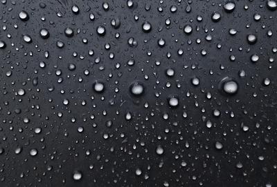 The primary subject of the image is a close-up of a rainy day, with a black background and a pattern of raindrops. The setting is a rainy day, and the visual style is a photo. The dominant colors are black and white, and the overall atmosphere is moody and atmospheric.