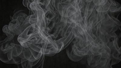 The primary subject of the image is a large, dark, and smoky cloud. The setting is a black background, which contrasts with the cloud, making it stand out. The visual style is a black and white photo, giving the image a dramatic and moody atmosphere. The dominant colors are black and white, with the cloud being the main focus of the image.