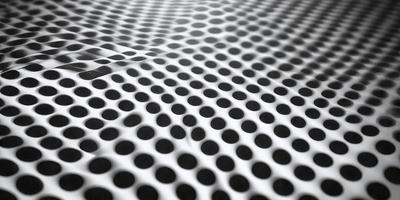 The primary subject of the image is a pattern of white dots on a black background. The setting is a white sheet or fabric, which serves as the backdrop for the pattern. The visual style is a close-up of the pattern, showcasing the intricate details of the dots. The colors and mood of the image are predominantly black and white, creating a clean and minimalist appearance.