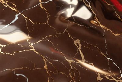 The primary subject of the image is a marble countertop with a gold-like pattern. The setting is a kitchen, and the visual style is a close-up of the marble countertop. The colors and mood of the image are warm and luxurious, with the gold-like pattern adding a touch of sophistication to the marble surface.