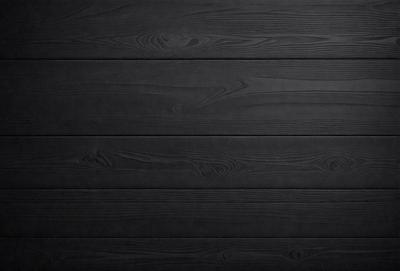 The primary subject of the image is a wooden wall. The setting is a black background, which creates a striking contrast with the wooden surface. The visual style is a close-up of the wooden wall, showcasing its texture and details. The colors and mood of the image are predominantly black, giving it a dramatic and moody atmosphere.