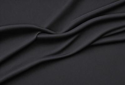 The primary subject of the image is a black fabric, which is the main object, scene, or focus of the image. The setting or background is a dark surface, and the visual style is a close-up of the fabric. The colors and mood of the image are predominantly dark, with the black fabric being the dominant color.