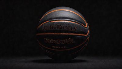 The primary subject of the image is a basketball. The setting is a dark room, and the visual style is a photo. The dominant colors are black and orange, and the overall atmosphere is intense and focused.