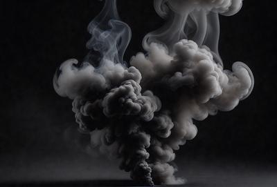 The primary subject of the image is a large, dark, and smoky cloud. The setting is a dark background, which contrasts with the cloud, creating a dramatic visual effect. The visual style is a black and white photo, which adds to the mood of the scene. The colors and mood of the image are dark and moody, emphasizing the intensity of the cloud.